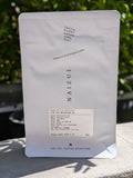 A 60g bag of NAIZUI coffee in a white stand-up pouch, photographed outdoors on a stone surface with blurred green foliage in the background.