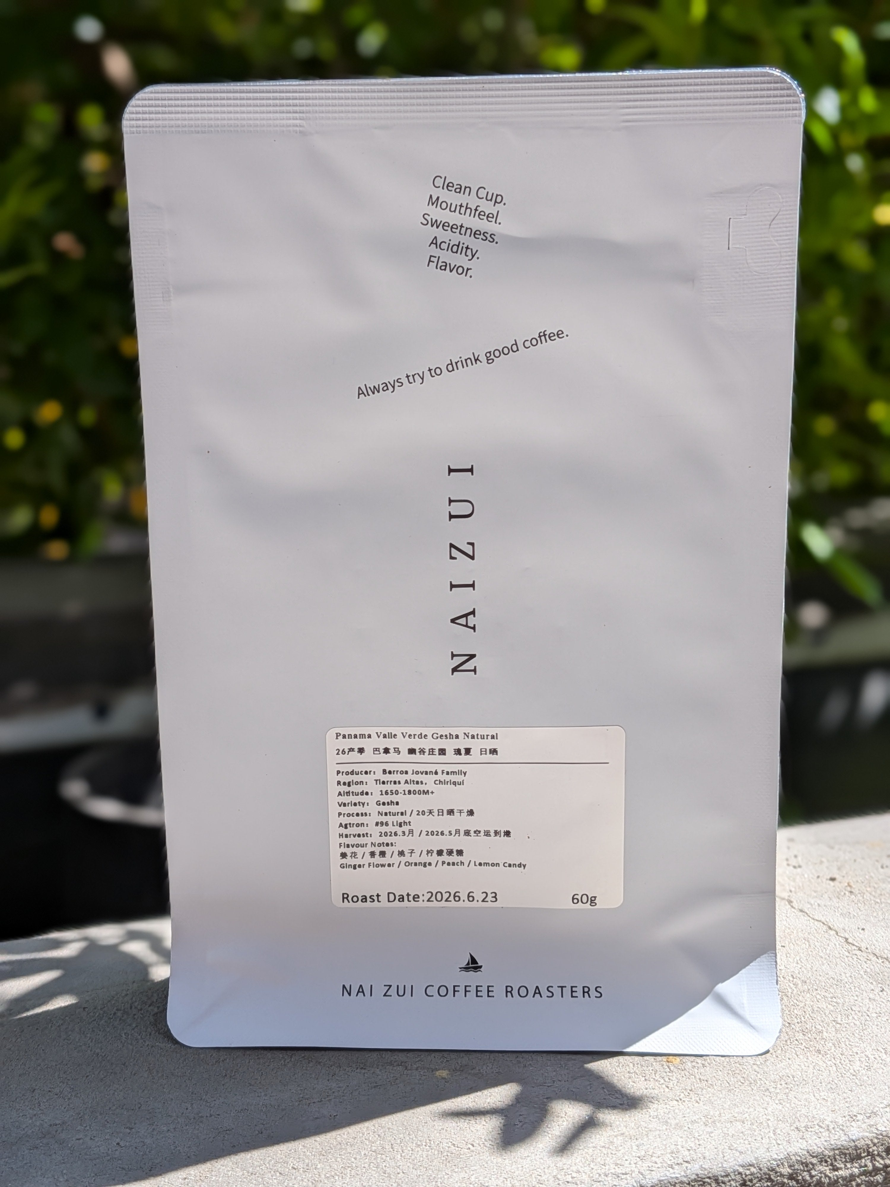 A 60g bag of NAIZUI coffee in a white stand-up pouch, photographed outdoors on a stone surface with blurred green foliage in the background.